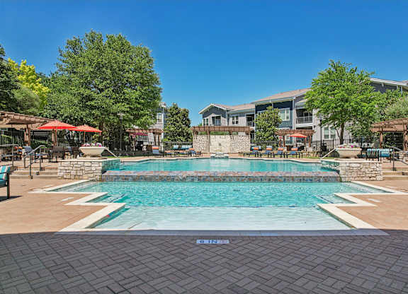 A large outdoor swimming pool surrounded by a stone wall and seating areas.