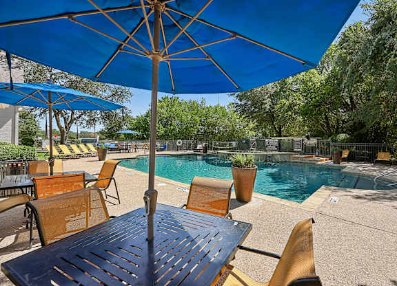 A pool area with a table and chairs under an umbrella.