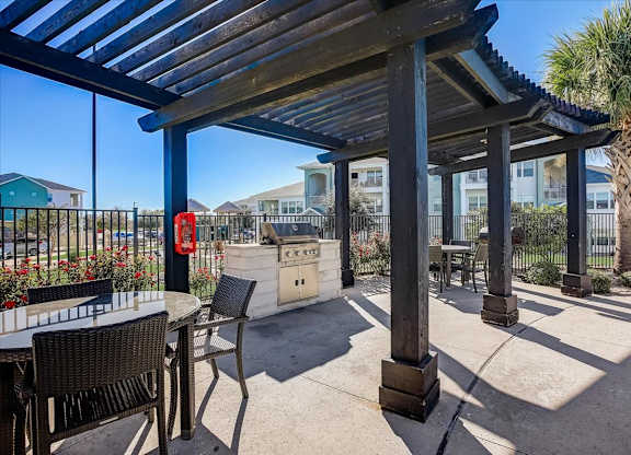 Pergola-covered patio dining area next to built-in grill station.