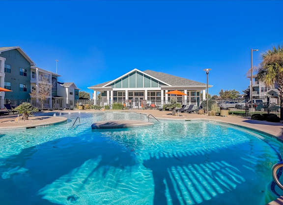 Resort-style pool with sun shelf, loungers, and clubhouse backdrop.