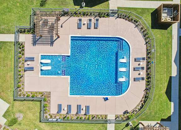 An aerial view of a swimming pool surrounded by a concrete patio and a grassy lawn.