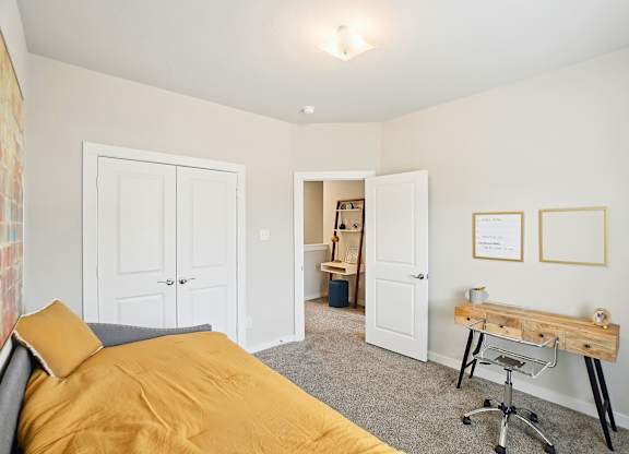A bedroom with a bed, desk, and two framed pictures on the wall.