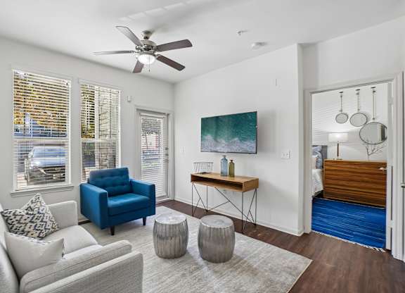 A living room with a white couch, blue chair, and a painting on the wall.