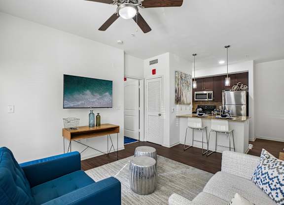 A blue couch sits in a living room with a painting on the wall and a bar area in the background.