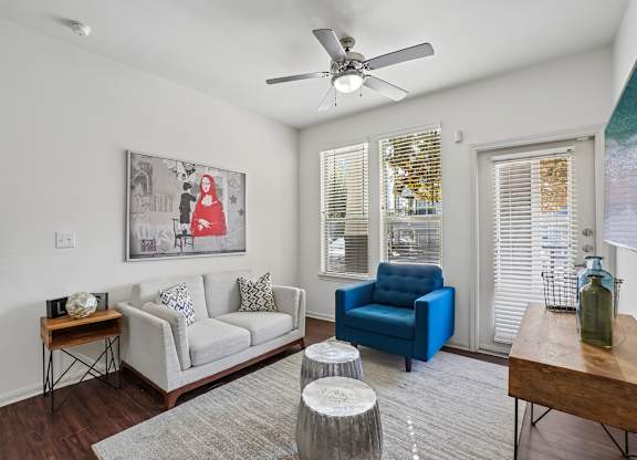 A living room with a white couch, a blue chair, and a painting on the wall.