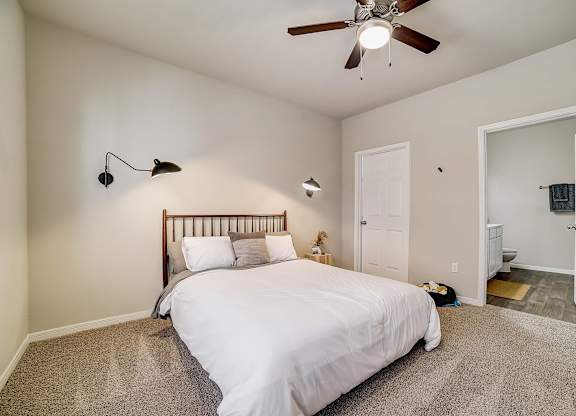 A bedroom with a bed, two lamps, and a ceiling fan.