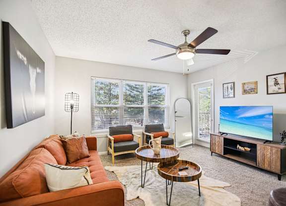 A living room with a brown couch, a TV, and a ceiling fan.