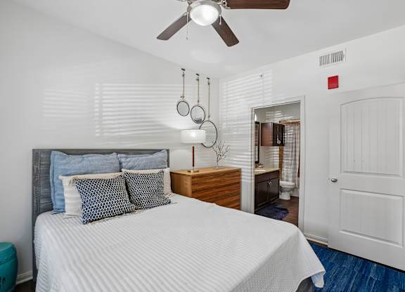 A bedroom with a bed, pillows, a ceiling fan, and a nightstand with a lamp.