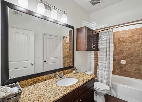 A bathroom with a sink, toilet, and a large mirror.