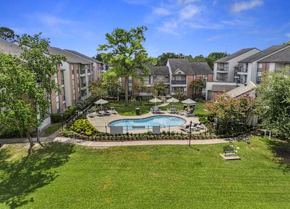 A swimming pool surrounded by grass and trees in a residential area.