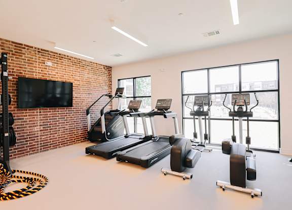 a gym with treadmills and weights and a wall of windows