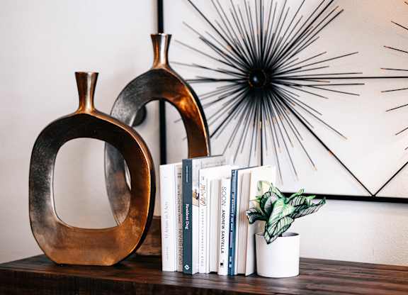 a shelf with two vases and books and a starburst mirror