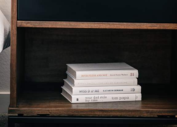 a stack of books on a nightstand with a clock and a drawer