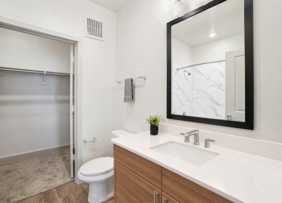Bathroom with quartz vanity, framed mirror, marble-look tiled shower, and adjoining walk-in closet.