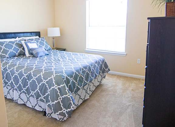 A bedroom with a bed, dresser, and window.