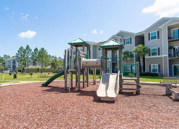 A playground with a green slide and a white slide in front of apartment buildings.
