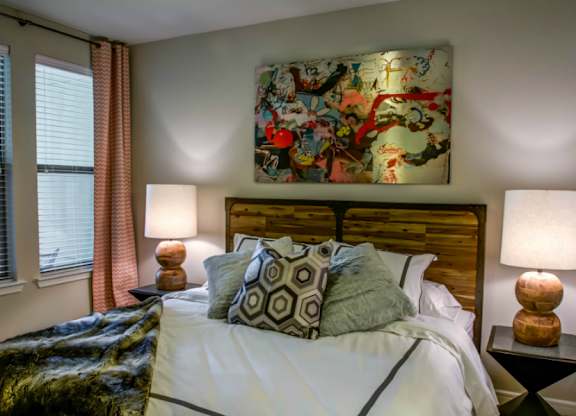 A bedroom with a large bed, two lamps, and a colorful painting on the wall.
