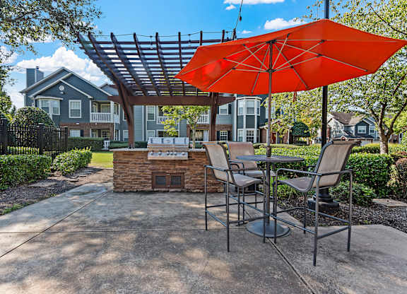 a patio with an umbrella and tables with chairs and a grill
