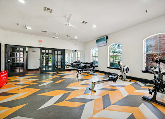 a gym with a colorful tile floor and bikes in a room with windows