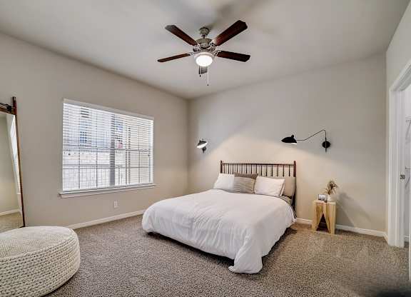 A bedroom with a bed, a ceiling fan, and a window with blinds.