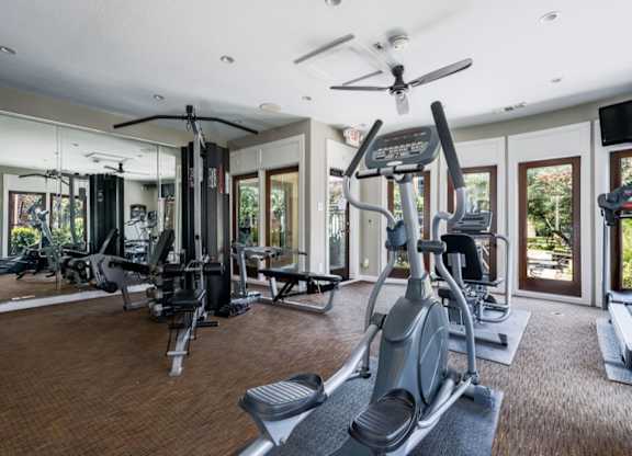 Spacious gym featuring mirrored wall, cable station, and cardio equipment by windows.