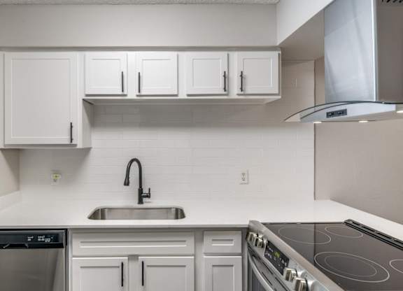White kitchen counter with undermount sink, white tile backsplash, and electric range.