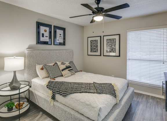 Serene bedroom with upholstered bed, ceiling fan, and large window blinds.