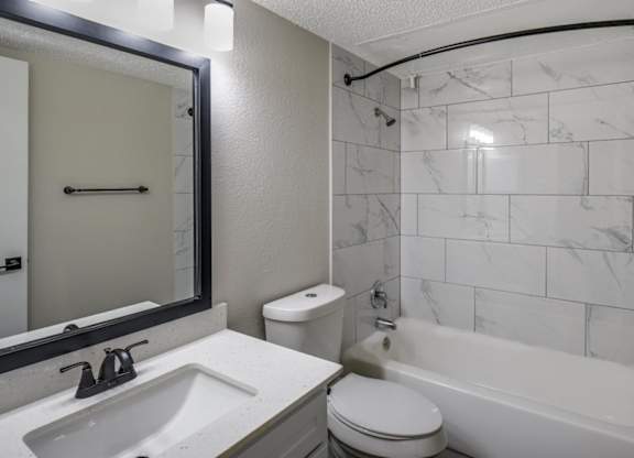 Bathroom with tub-and-shower combo, marble-look tile surround, and single-sink vanity.