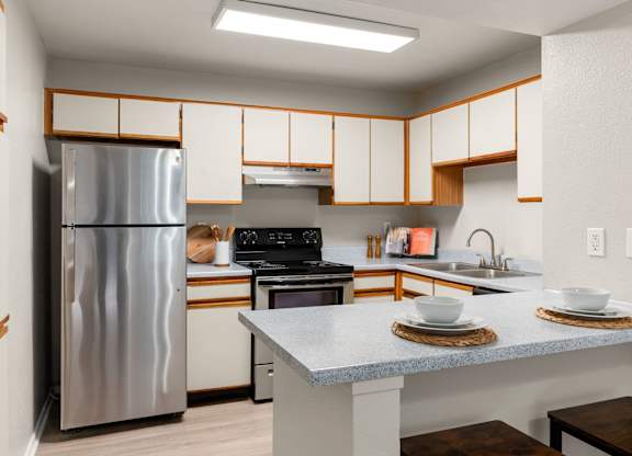 Classic kitchen with white cabinetry, breakfast bar, and stainless steel refrigerator at Heritage at Valley Ranch, Irving, TX.