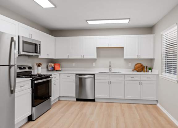 Spacious renovated kitchen with white shaker cabinets, stainless steel appliances, and wood-style flooring.