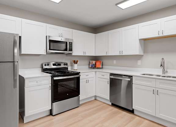 Updated apartment kitchen with wraparound counters, white cabinetry, and stainless steel dishwasher and range.