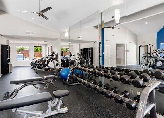 Spacious fitness center with free weights, cardio machines, mirrored wall, and vaulted ceiling.