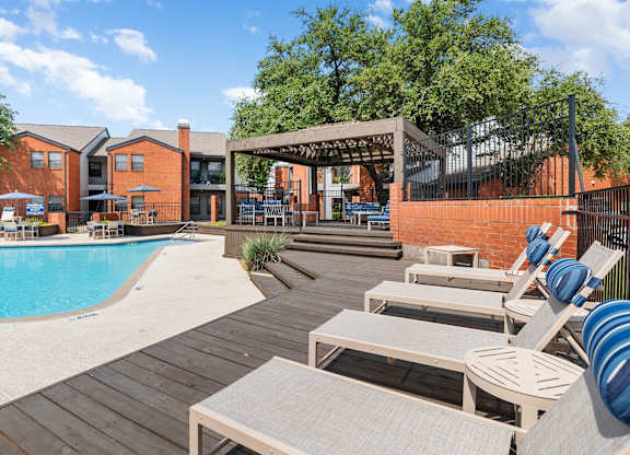 Pool deck with lounge chairs, pergola seating, and landscaped surroundings at Heritage at Valley Ranch.