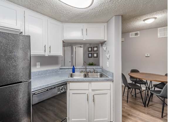 A kitchen with a black refrigerator, white cabinets, and a wooden table.