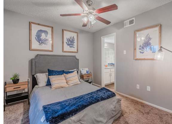 A bedroom with a bed, a ceiling fan, and three wall art pieces.