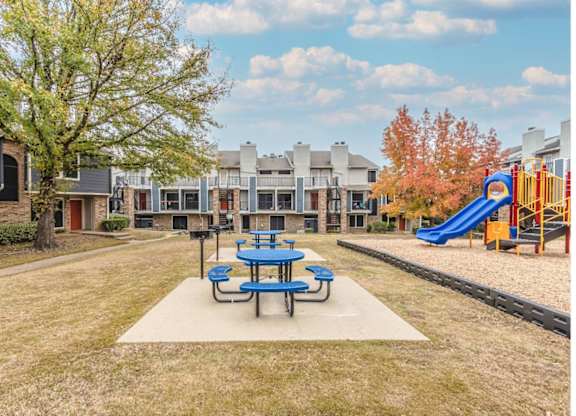 A playground with a blue slide and picnic table in the foreground.
