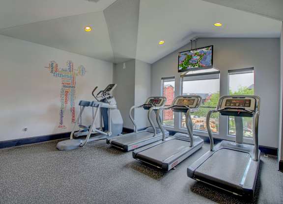 a workout room with treadmills and a tv
