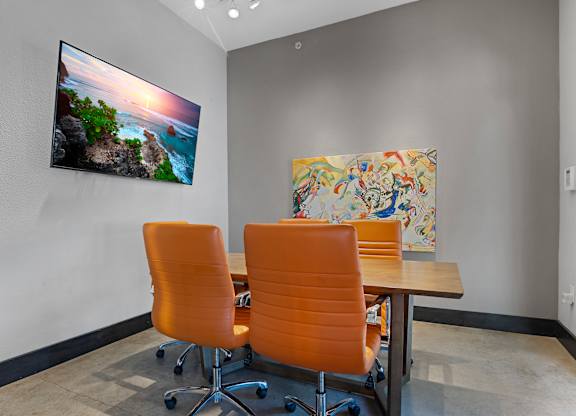 Two orange chairs are placed in front of a table with a painting and a picture on the wall.