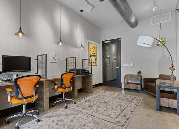 A room with a desk, chairs and a rug.