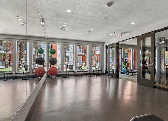 A gym with a mirrored wall and a row of exercise balls.