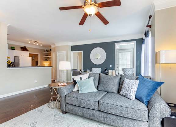 A grey couch with blue pillows is in the center of a room with a ceiling fan.