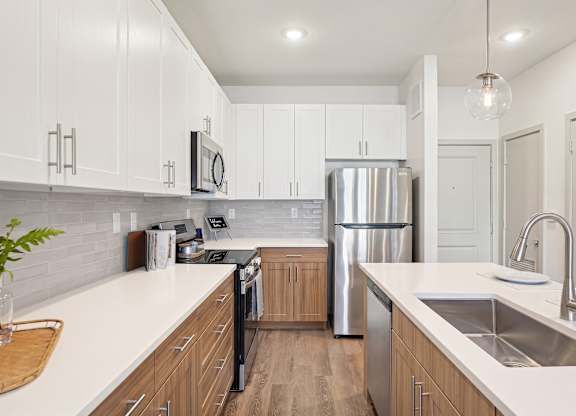 Galley kitchen with light solid-surface island, tile backsplash, stainless-style appliances, and two-tone white and wood cabinetry.