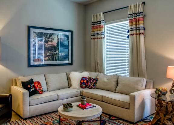 A living room with a beige couch, a coffee table, and a painting on the wall.