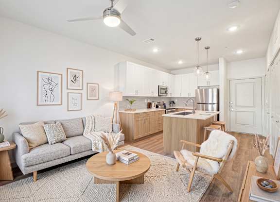 Open-concept living room at Cedar Grove Apartment Homes with ceiling fan, plank flooring, and adjoining kitchen island seating.