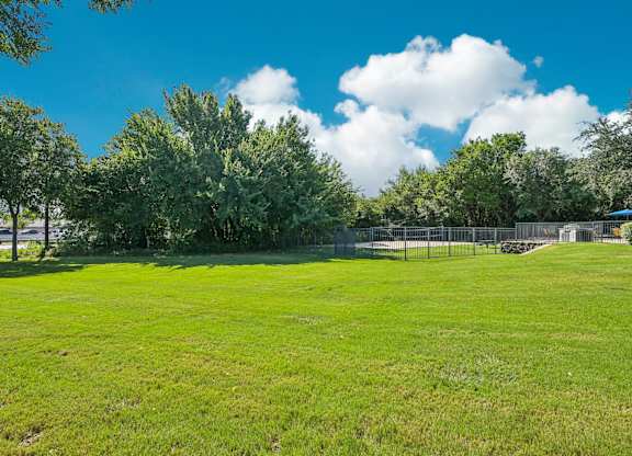 a large grassy field with a tennis court and trees