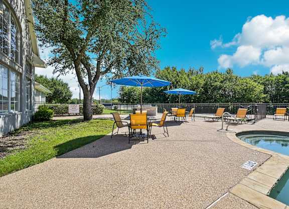 a patio with chairs and umbrellas next to a pool