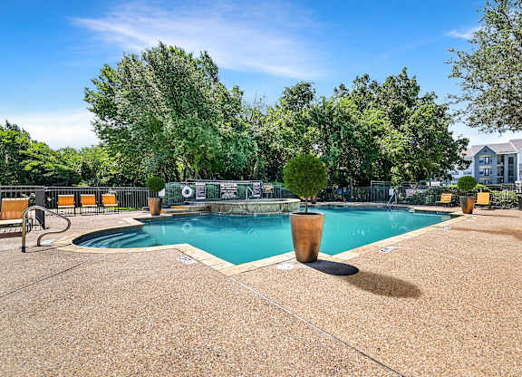 A large outdoor swimming pool surrounded by trees and lounge chairs.