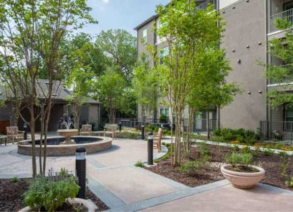 a courtyard with a fountain and trees in front of an apartment building