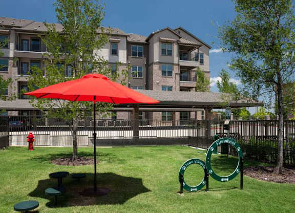 a park with a red umbrella in front of an apartment building