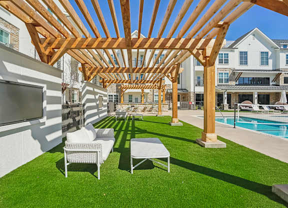 a backyard with a pool and a wooden pergola with chairs and a television